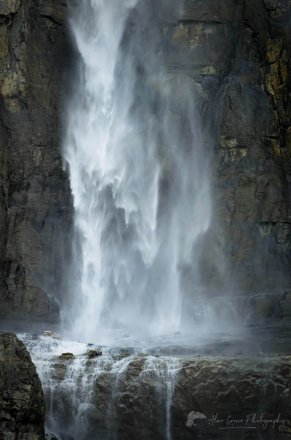 a large waterfall is in the middle of some trees and mountains with snow on top